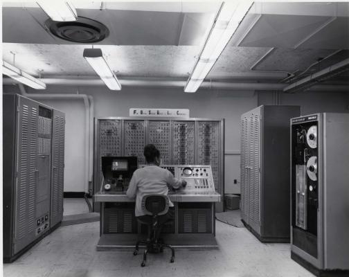 An African-American woman sits at the console of a FOSDIC (Film Optical Sensing Device for Input to Computers) device inputting data